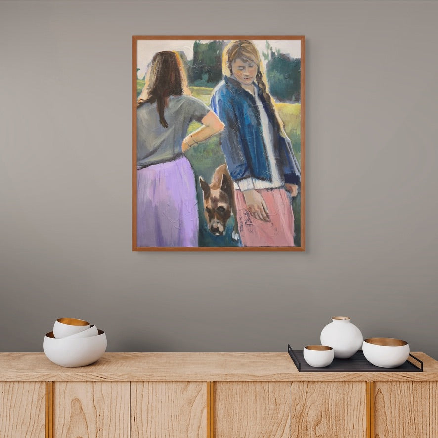 Framed artwork of two people with a dog on a gray wall above a wooden console table with decorative items.